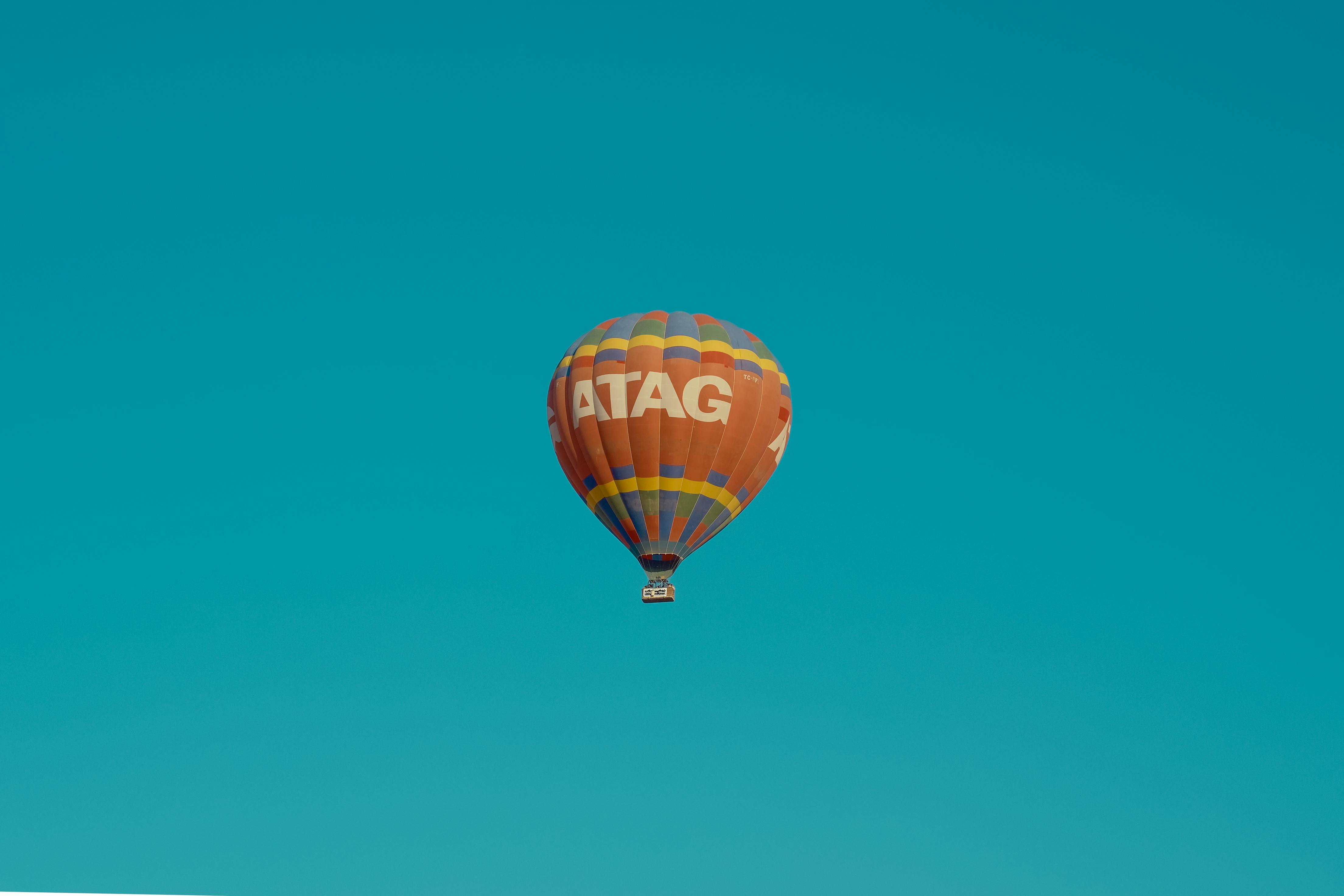 an orange hot air balloon in mid air under clear blue sky