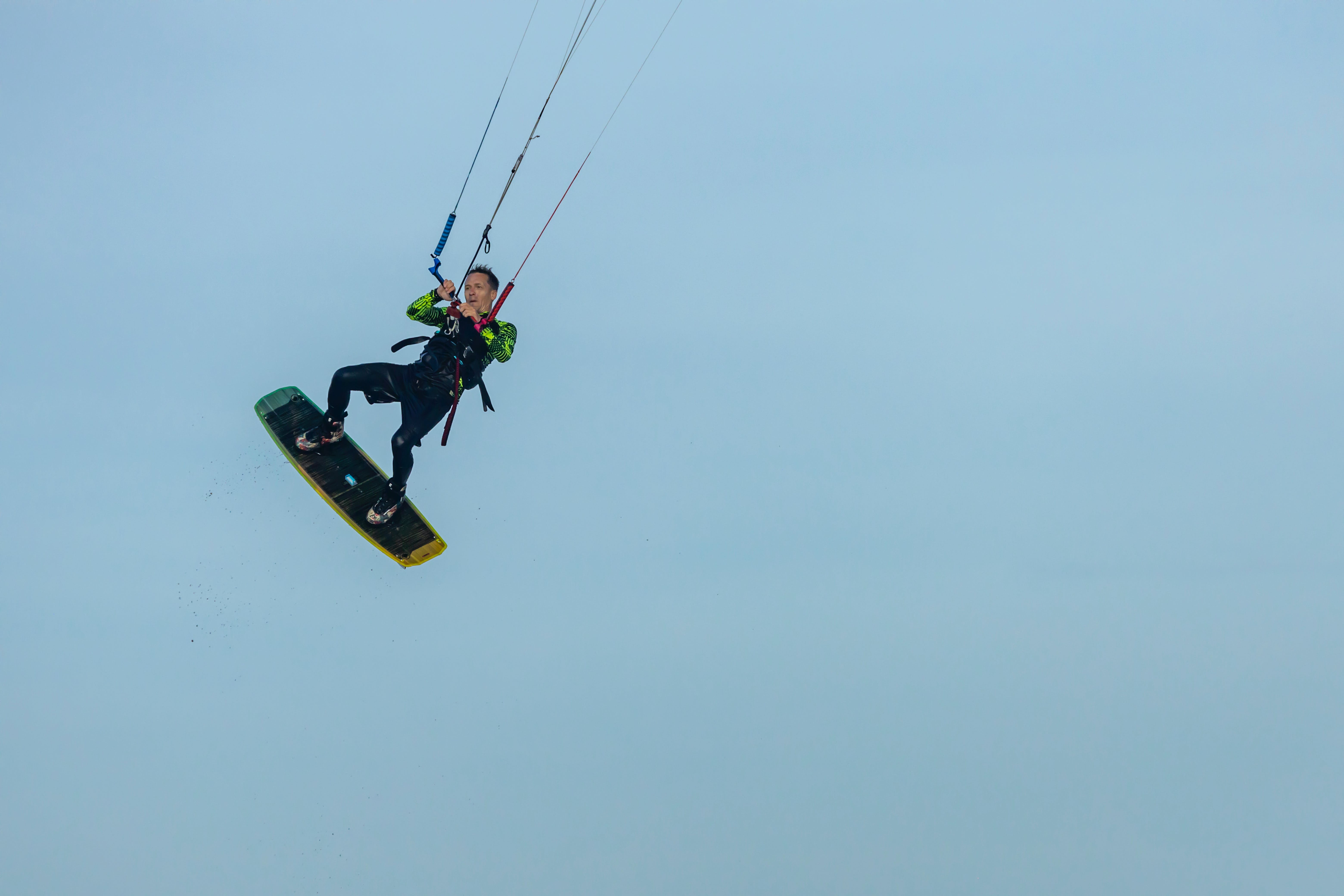 a man in black and green shirt riding in the air a kite surf board on blue sky