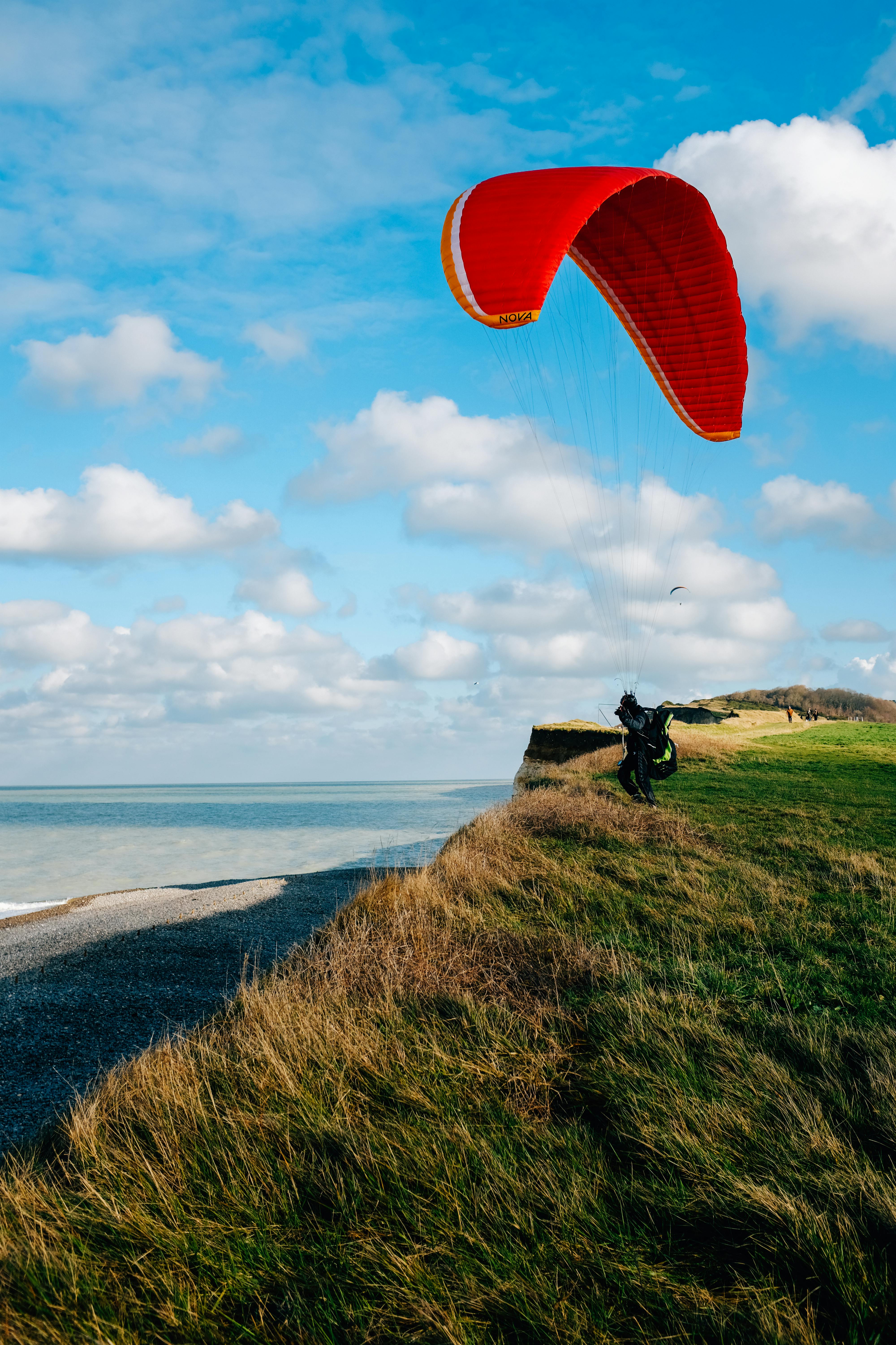 anonymous paraglider landing on grassy seashore