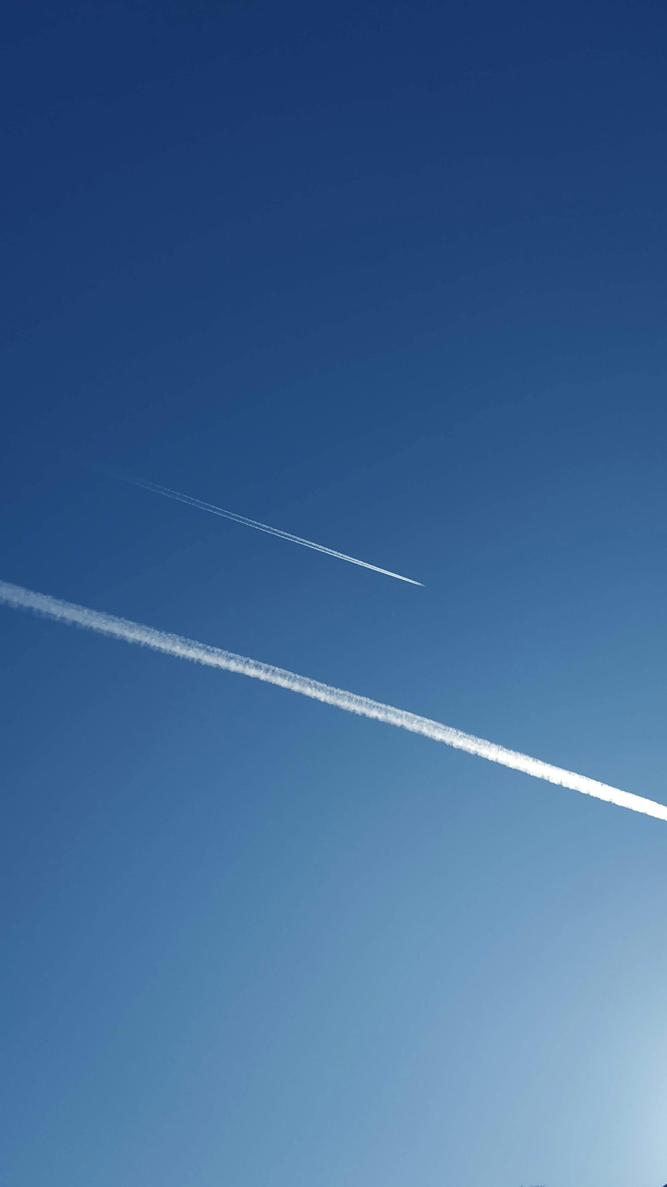 airplanes with condensation trails flying in blue cloudless sky